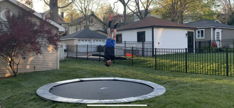 Person performing a backflip on a circular in-ground trampoline in a residential backyard