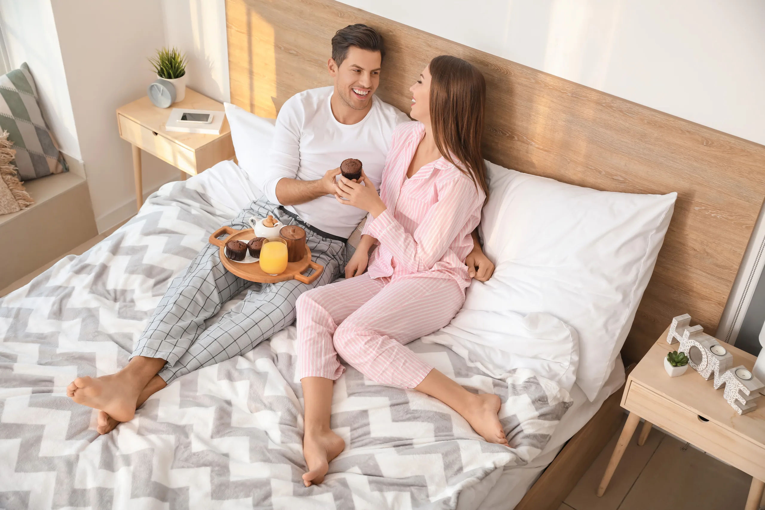 Couple enjoying breakfast in bed with matching wood nightstands aligned flush with the mattress sleeping surface